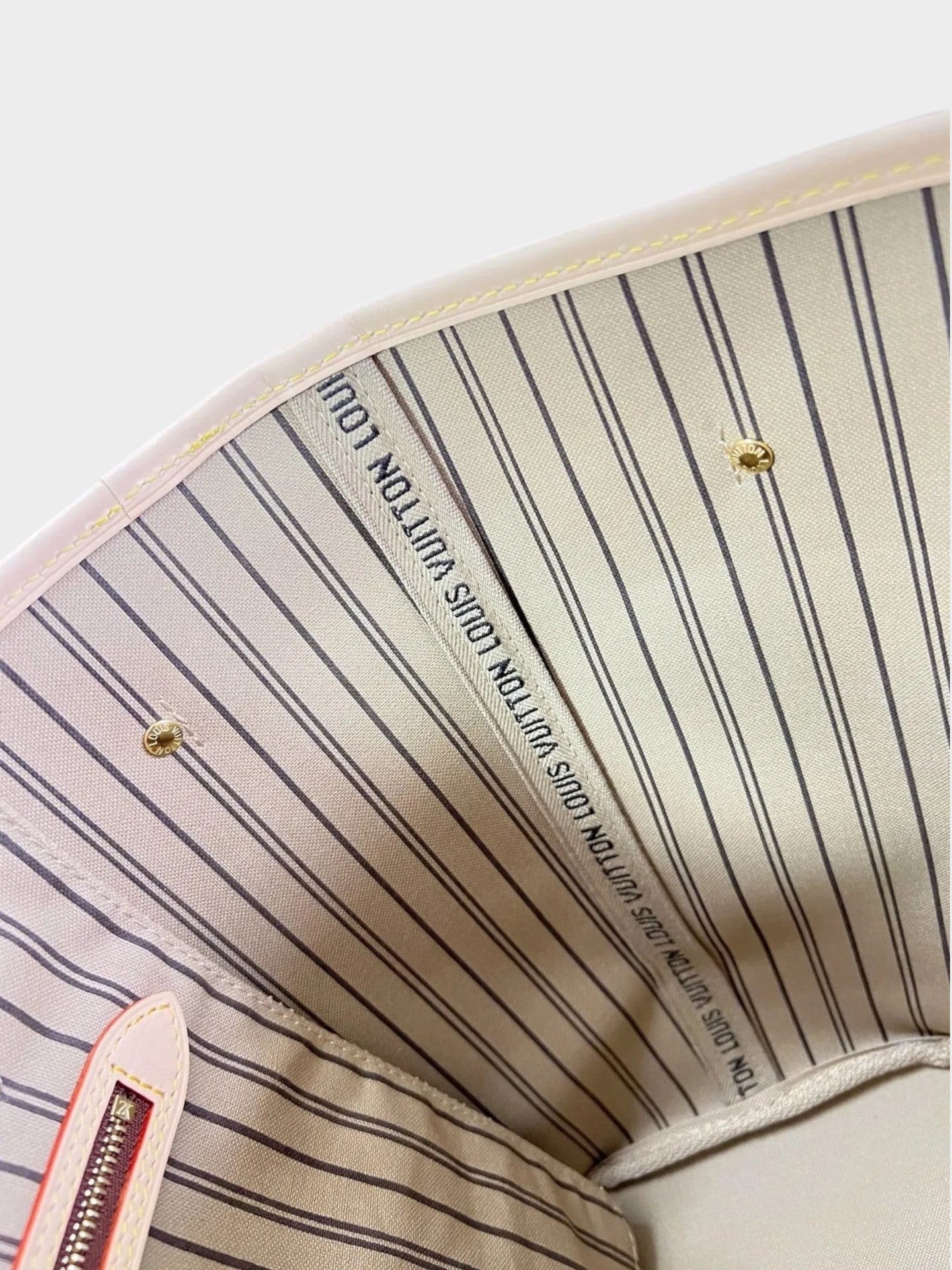Zebass LOUIS VUITTON Neverfull tote bag interior featuring beige striped fabric lining and gold-tone hardware details.