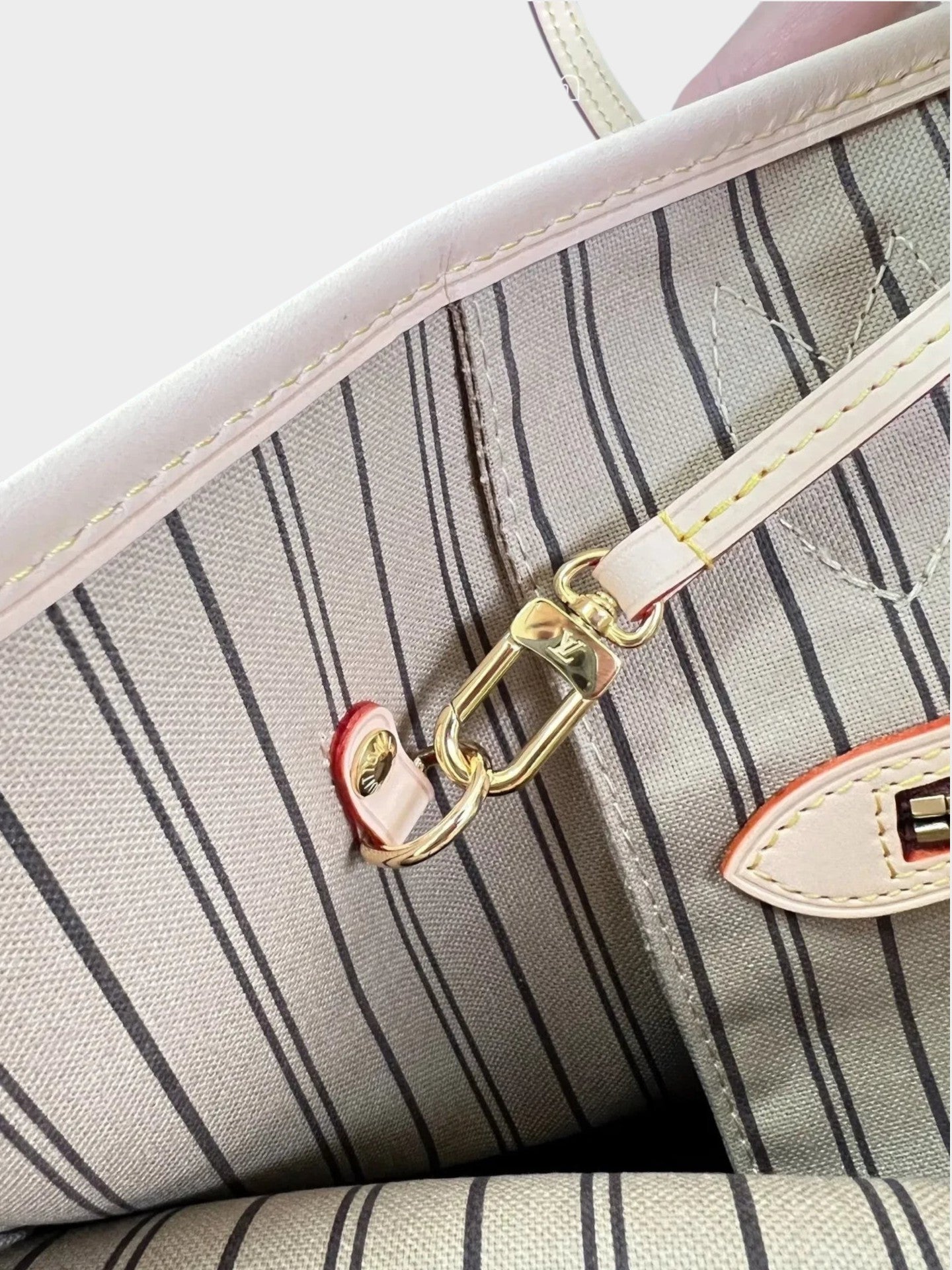 Zebass LOUIS VUITTON Neverfull tote bag interior with striped fabric lining, leather trim, and gold-tone lobster clasp.