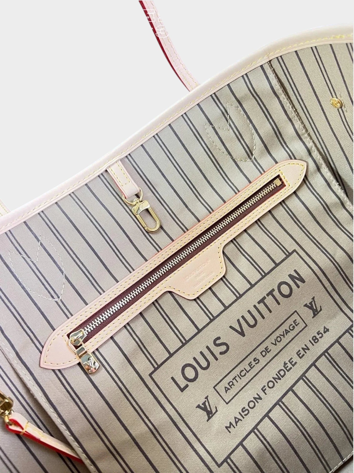 Zebass LOUIS VUITTON Neverfull tote interior featuring striped fabric lining, zippered pocket, and gold-tone hardware.